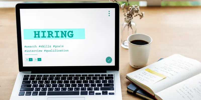 tea and books besides a laptop with screen showing word hiring 